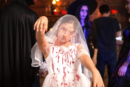 Portrait of little girl dressed up like a bride covered with blood at halloween party. Girl with...