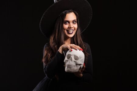 Beautiful woman dressed as witch for Halloween playing with a scary skull. Brunette witch doing magic with a skull.の写真素材