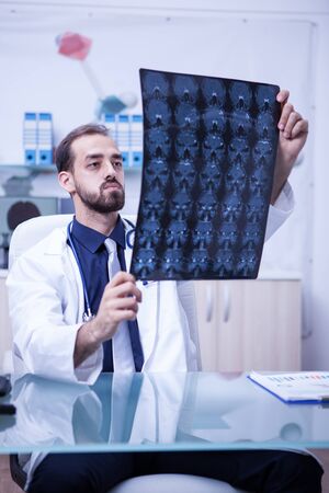 Young doctor at the clinic cabinet holding a brain radiography. Doctor checking the brain scan of a patient.の写真素材