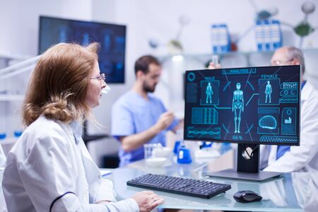 Female scientist looking at the monitor screen in research room. Chief of development working with test tubes in the background.の写真素材
