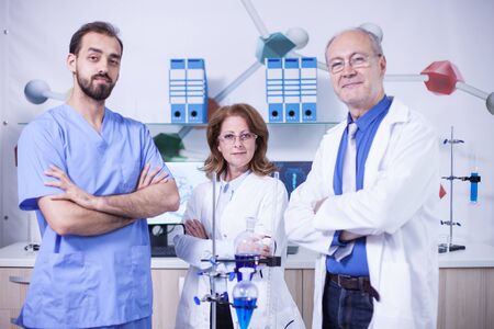 Portrait of three scientist dressed in their uniform in a laboratory. Senior scientist in white coat.の写真素材