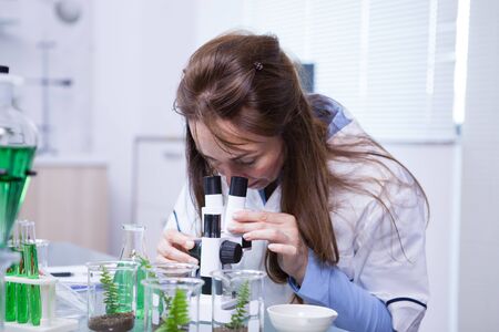 Middle age female scientist looking through a microscope in a research lab. Biotechnology research...
