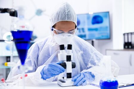 Chemist with safety glasses looks in the microscope and adjusts it