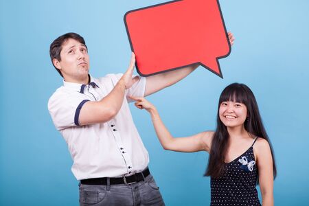 Asian girlfriend pointing at his caucasian boyfriend while he is holding an empty sign. Interracial...