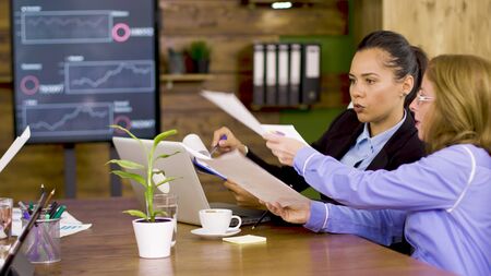 Two business women in the conference room looking at firm statistics report.