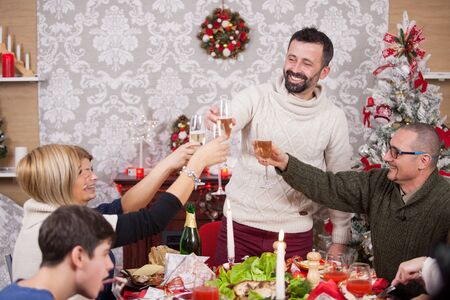 Cheerful family portrait making a toast with champagne at christmas feast. Delicious and traditional foood for christmas feast. Christmas decoration. Christmas tree. Family sitting around the table.の写真素材