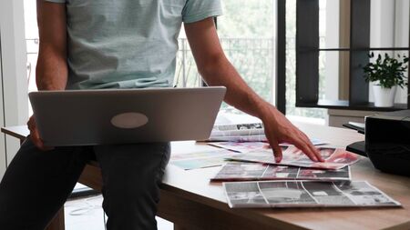 Close up with the hands and feet of a young designer working on a laptop. Photos printed on the...