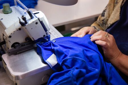 Close up with hands on a woman working on a sewing machine. Blue textil materialの写真素材