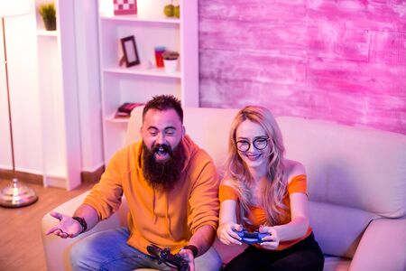 Boyfriend cant believe his girlfriend is winning at online video games. Couple sitting on sofa. Neon light in the room.の写真素材