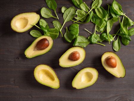 Top view of avocado next to baby spinach on dark wooden boardの写真素材