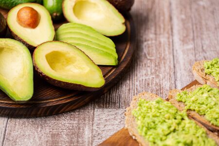 Avocado sandwiches next to cutted ones on wooden board.の写真素材
