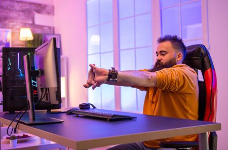 Bearded man sitting on gaming chair preparing to play online video games on pc. Room with colorful neons.の写真素材