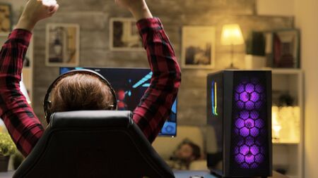 Back view of woman winning at video games while playing late at night. She has a powerful PC with...