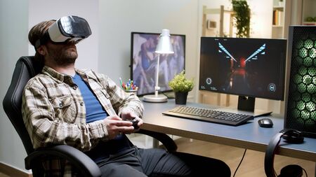 Bearded man sitting on gaming chair playing games using vr headset. Woman in the background.の写真素材