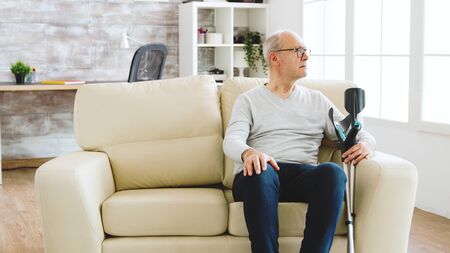 Revealing shot of male nurse checking on retired old man with alzheimer sitting on a couch in the nursing homeの写真素材