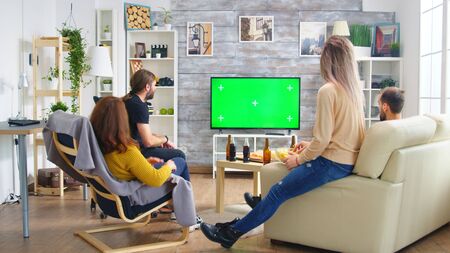 Back view of close friends with hands in the air while watching a football match in living room.の写真素材