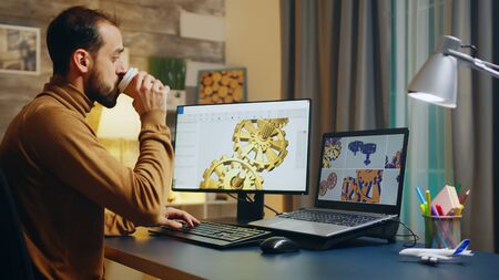 Bearded engineer taking a sip of coffee while working on computer.
