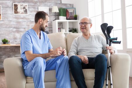Elderly age man smiling while talking with male doctor in nursing home while holding crutches.の写真素材