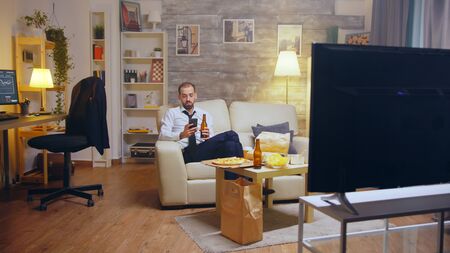 Young businessman in suit and tie relaxing drinking beer and browsing on phone after a hard day at...