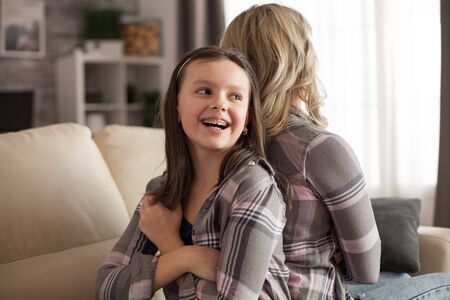 Little girl with a big smile and braces sitting back to back with her mother upset on her. Disobedient kidの写真素材