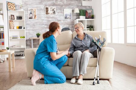 Happy old woman in a nursing home sitting on couch talking with her caretaker. Retired woman with crutches.の写真素材