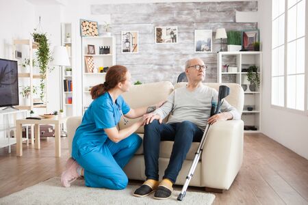 Pretty nurse trying to get old man attention in nursing home. Old man with crutches.の写真素材