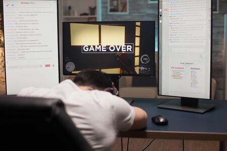 Back shot of upset young man over his loss at playing online shooter games on computer. Game over for young man.の写真素材