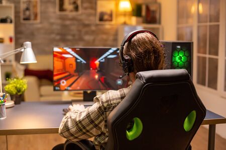 Back view of gamer male playing a shooter on his powerful PC computer late at night in the living room.の写真素材