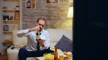 Businessman with tie eating noodles sitting on couch after a long day at work. Chinese food.の写真素材