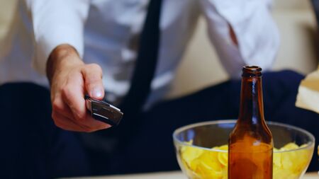 Close up of businessman sitting on couch using remote control. Beer on table.の写真素材