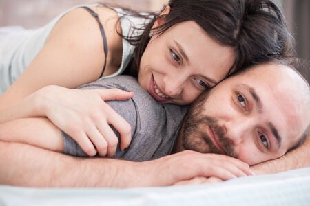 Close up of beautiful woman smiling after waking up in the morning and laying on her boyfriend back.の写真素材