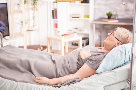 Sick old woman lying in nursing home bed. Lonely woman.の写真素材