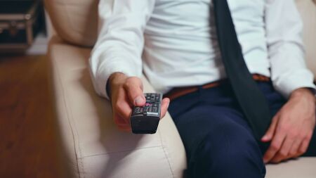 Businessman at home in formalwear and a tie resting and using tv remote control.の写真素材