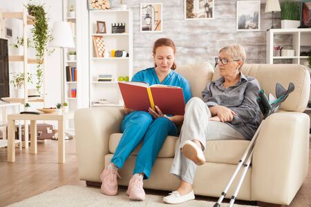 Doctor with blue uniform reading a book for senior woman in retirement home.の写真素材