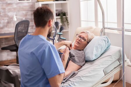 Back view of male doctor using stethoscope to check woman heart in nursing home.の写真素材