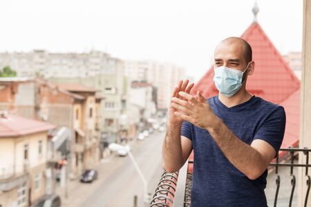 Adult man with protection mask clapping on balcony showing support for medical staff on fight with coronavirus.の写真素材