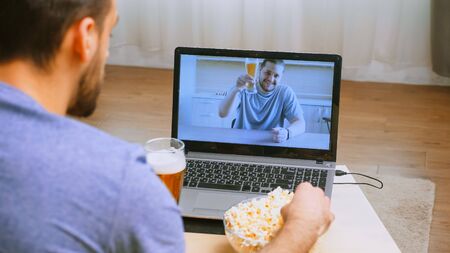 Man waving at his friend during a video call in timp of covid-19 and beer on the table.の写真素材
