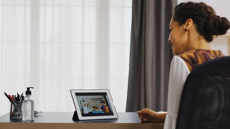 Excited woman waving at her family during a video call on tablet computer.