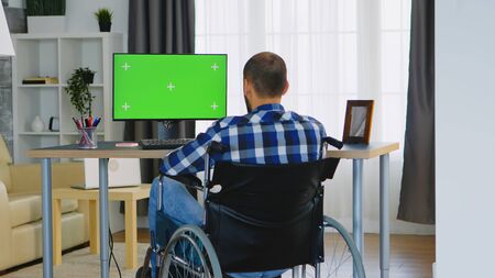 Businessman in wheelchair in front of computer with green screen.の写真素材
