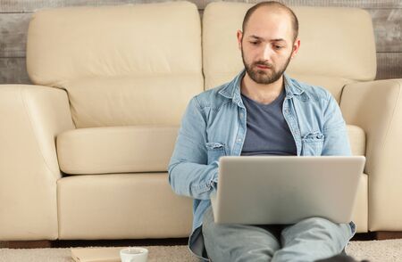 Adult man using laptop sitting on living room carpet.の写真素材