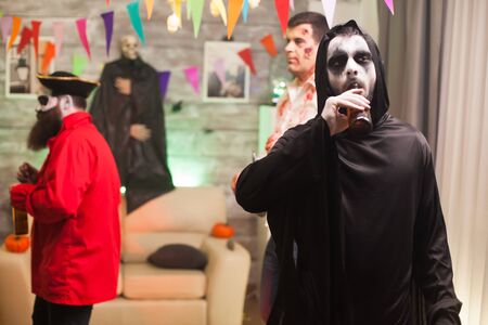 Grim reaper enjoying his beer at halloween celebration. Scary man.の写真素材