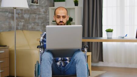 Invalid man in wheelchair working on laptop from home.