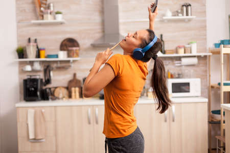 Cheerful woman singing in the kitchen in the morning. Energetic, positive, happy, funny and cute housewife dancing alone in the house. Entertainment and leiuse alone at homeの写真素材
