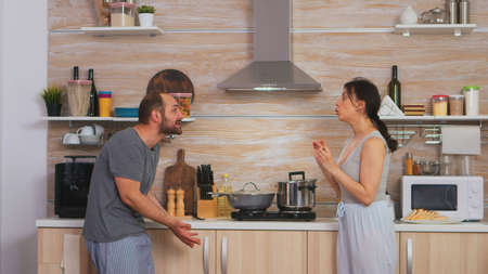 Couple screaming at each other in the kitchen in the morning. Young couple quarrels in the kitchen. Man and woman screams in frustration during home conversation.の写真素材