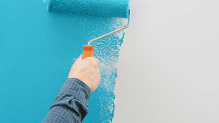 Man painting wall with blue paint using roller. Construction worker, tool, apartment renovation.の写真素材