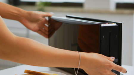 Wife roasting bread slices on electric toaster for breakfast meal. Housewife using bread toaster for...