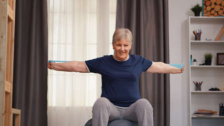 Old woman doing physical training sitting on fitness ball. Old woman lifting training healthy...