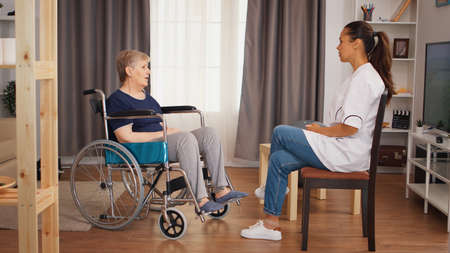 Disabled senior woman in wheelchair talking with doctor. Old person retirement home, healthcare nursing, health support, social assistance, doctor and home serviceの写真素材