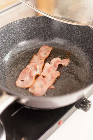 Fried bacon in the pan for a delicios breakfast. Healthy morning in cozy interior, delicious home meal preparation.の写真素材