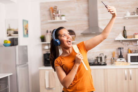 Young woman having a good day, taking a selfie in the kitchen. Energetic, positive, happy, funny and cute housewife dancing alone in the house. Entertainment and leiuse alone at homeの写真素材